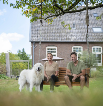 Eigenaren met hond zitten voor hun monumentale boerderij